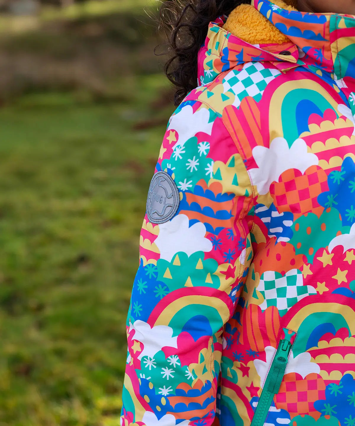Child wearing the Frugi snow and ski coat in the fun frenzy design showing a close up of a brand patch on the upper arm