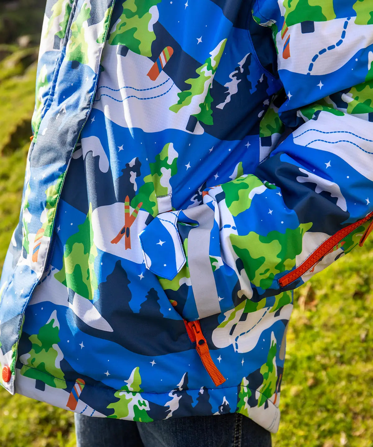 Child wearing the Frugi recycled polyester snow and ski coat in starry slopes showing a close up of the zipped pocket on the arm 