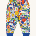 Frugi Snuggle Crawlers - Retro Happy. A fun retro print pair of trousers with a soft, double layer on the knees to protect crawling children. They also have stretchy rib ankle cuffs, an elasticated waistband, and an adjustable drawcord on the waist. The pattern on these trousers is smiling planets, flowers, stars, bees, butterflies, clouds and rainbows