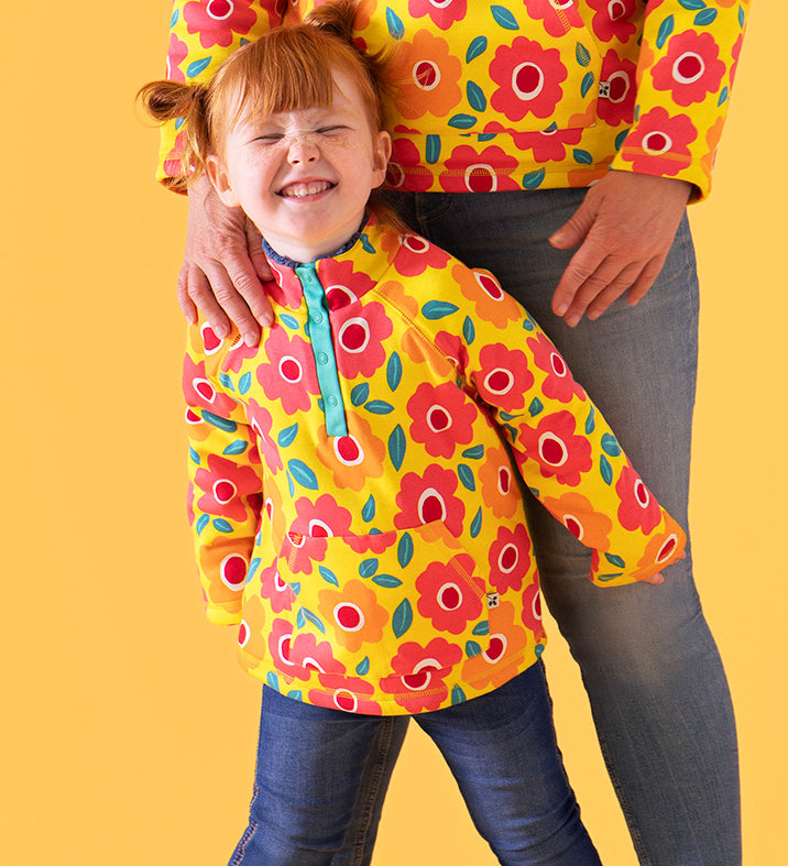 Child wearing Frugi's organic cotton snuggle fleece in yellow with repeating bright flower design prints.