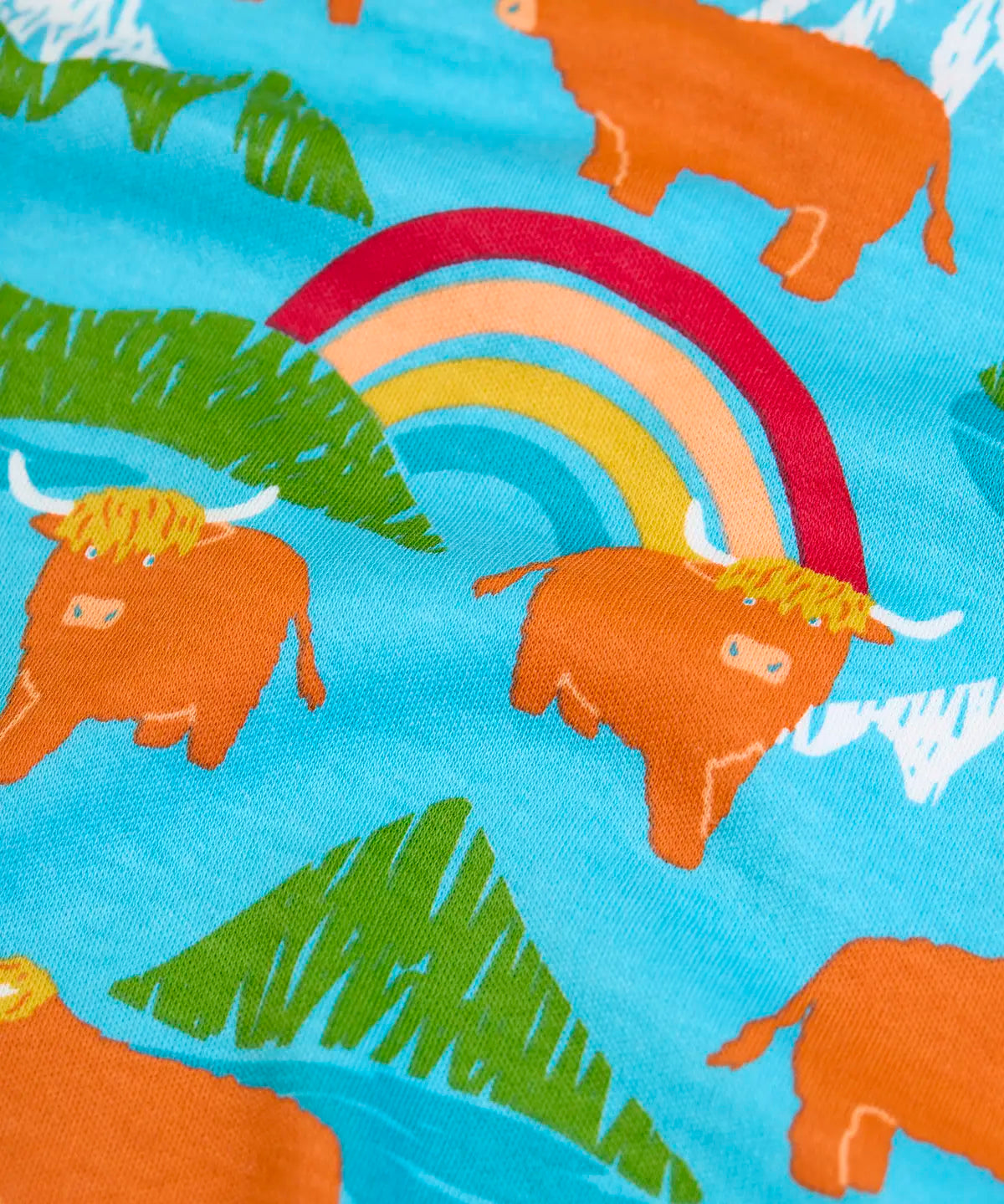 Frugi long sleeve skater dress showing a close up of the repeating mountain peaks, rainbows and highland cow print on light blue organic cotton fabric