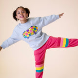 A child posing and wearing the Frugi Superb Stitched Skateboard sweatshirt with the Frugi rose/rainbow applique joggers available at Babipur.
