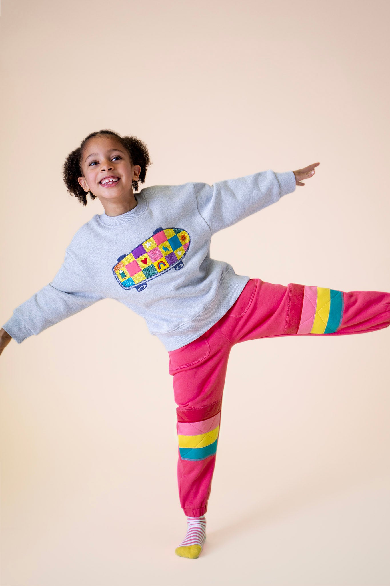 A child posing and wearing the Frugi Superb Stitched Skateboard sweatshirt with the Frugi rose/rainbow applique joggers available at Babipur.