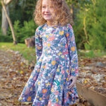 A child happily stood outside on a path with crunchy autumn leaves, wearing the Frugi Sofia Skater Dress - Rainforest Friends