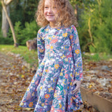 A child happily stood outside on a path with crunchy autumn leaves, wearing the Frugi Sofia Skater Dress - Rainforest Friends