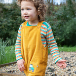 A child outside, wearing the Frugi Adley Cord Dungarees - Gold/Tractor