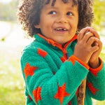 A child outside in the sun, wearing the Frugi Zipped Ted Fleece Jacket - Bonfire Stars
