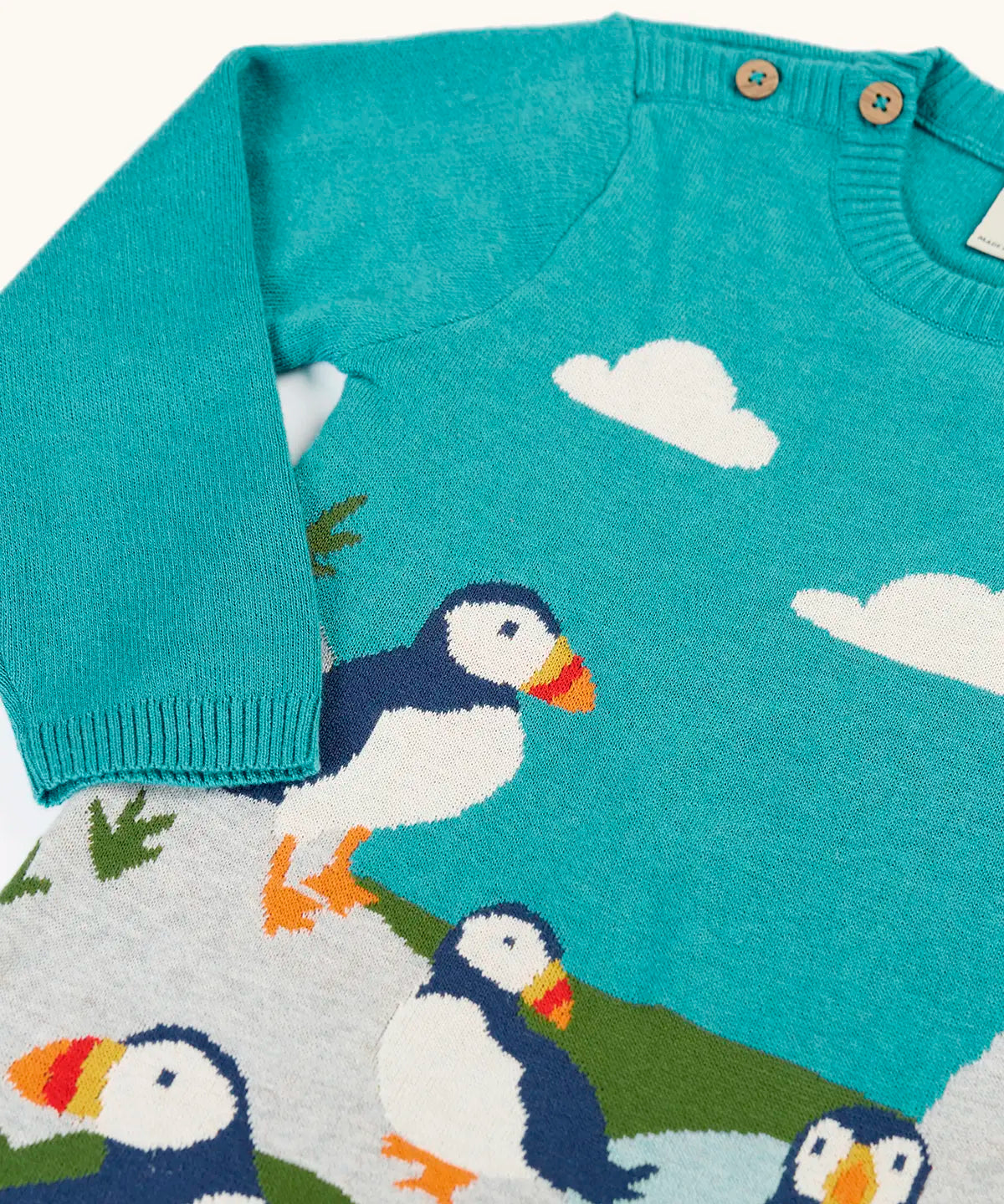 Frugi kids knitted dress in light blue laid flat showing a close up of the elasticated cuffs and button fasteners on the shoulder