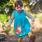 A child playing outside and wearing the Frugi Lily cord dress in boat blue available at Babipur. A GOTS organic cotton dress in light blue with a playful fox appliqué on the frill of the dress.