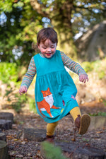 A child playing outside and wearing the Frugi Lily cord dress in boat blue available at Babipur. A GOTS organic cotton dress in light blue with a playful fox appliqué on the frill of the dress.