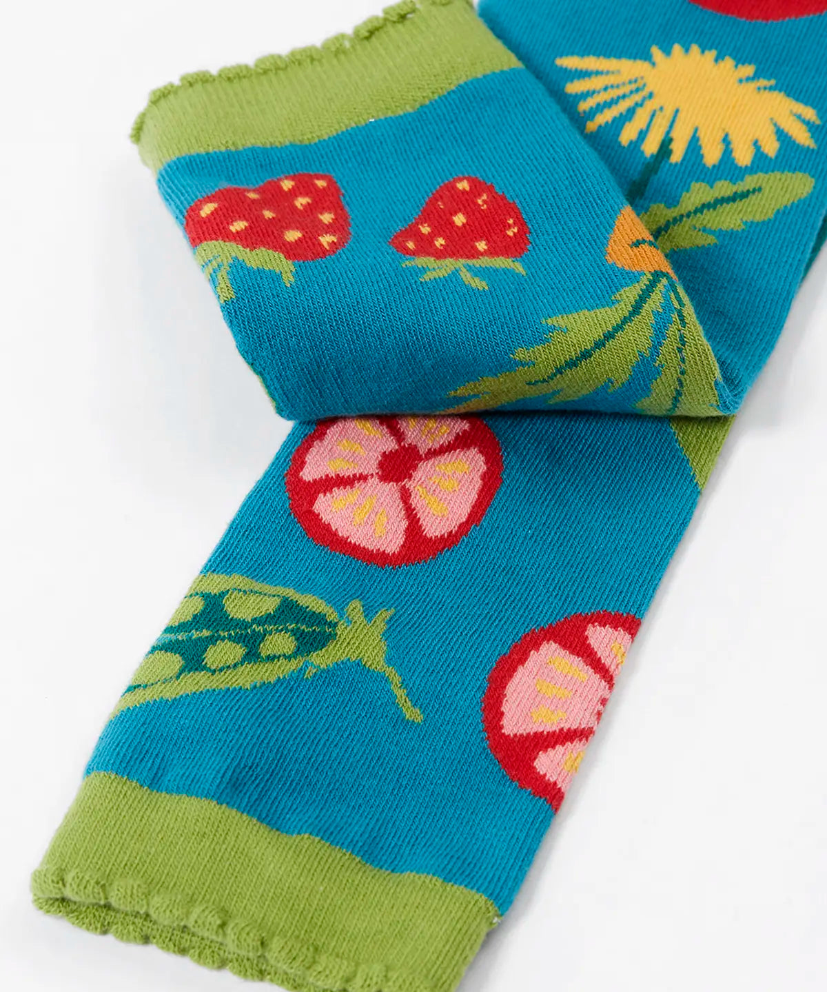 Frugi knitted leggings in light blue showing a close up of a repeating vegetables design on the leg and frilled green cuff on light blue organic cotton fabric