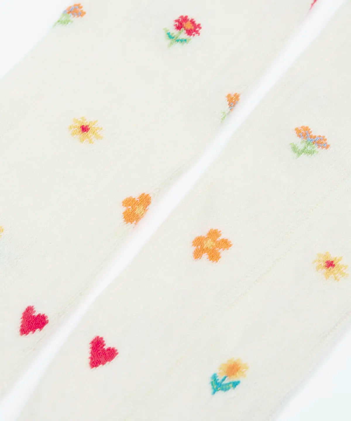 Pair of Frugi little pointelle kids tights in soft white laid flat showing a close up of the repeating floral and heart design on white organic cotton fabric