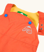 Frugi little waterproof dungarees in fire orange laid flat showing open popper fastener on the shoulder strap for size adjustment