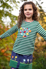 A child standing outside and wearing the Frugi Louise embroidered top in green breton / heart. A GOTS organic cotton top available at Babipur in green and white stripe with a collection of embroidered flowers shaped as a heart
