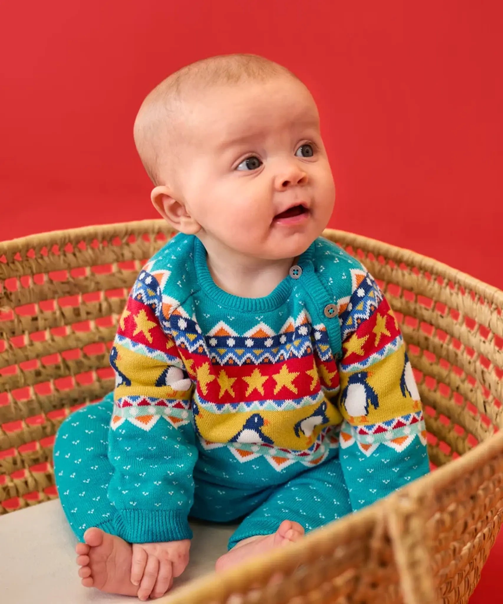 Baby wearing the Frugi GOTS 100% organic cotton knitted rompersuit in blue with a winter themed fairisle design on the upper half. Features elasticated cuffs and shoulder buttons for easy dressing.