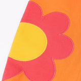 Frugi GOTS 100% organic cotton salamander orange organic joggers laid flat showing a close up pink flower applique on the lower leg