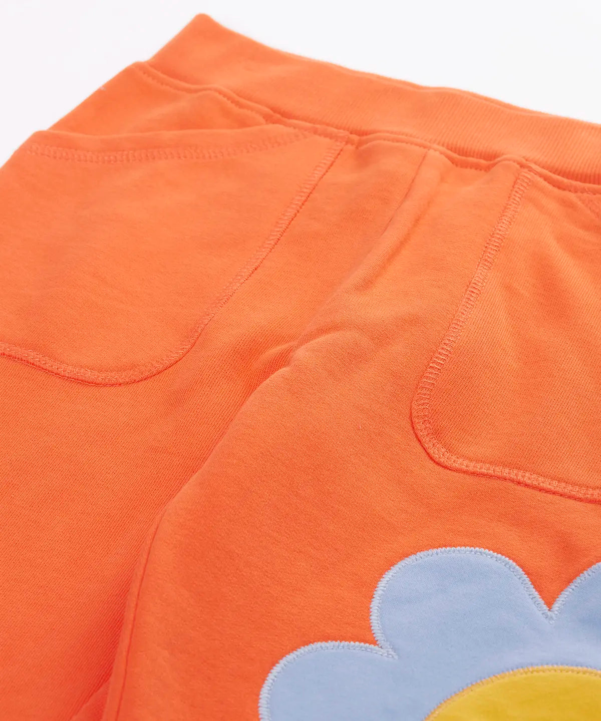 Frugi GOTS 100% organic cotton salamander orange organic joggers laid flat showing a close up of the side pockets and elasticated waist band
