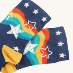 The navy blue pair of socks from the Frugi Rock My Socks - Stars 2 Pack. These navy socks have a rainbow wavy print on them with white stars, and white stars on the ankle cuffs