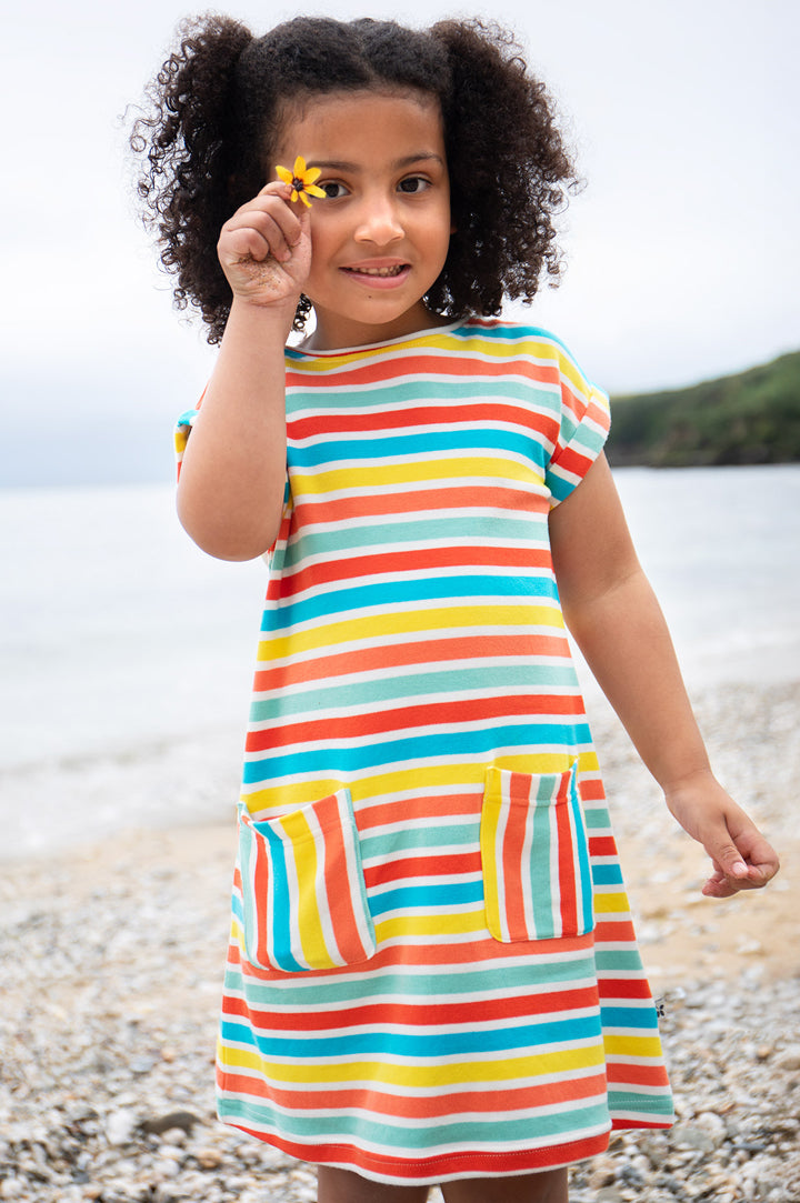 Child on beach wearing Frugi Organic cotton dress with rainbow stripes and two pockets