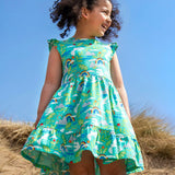 Child wearing Frugi's skater dress in aqua with a repeating seagull and mountain design on the beach 