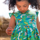 Child wearing Frugi's skater dress in aqua with a repeating seagull and mountain design and frilled shoulders