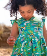 Child wearing Frugi's skater dress in aqua with a repeating seagull and mountain design and frilled shoulders