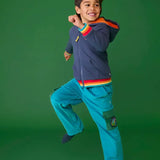 Frugi adventure trousers in boat blue with navy hoodie and rainbow cuffs worn by boy.