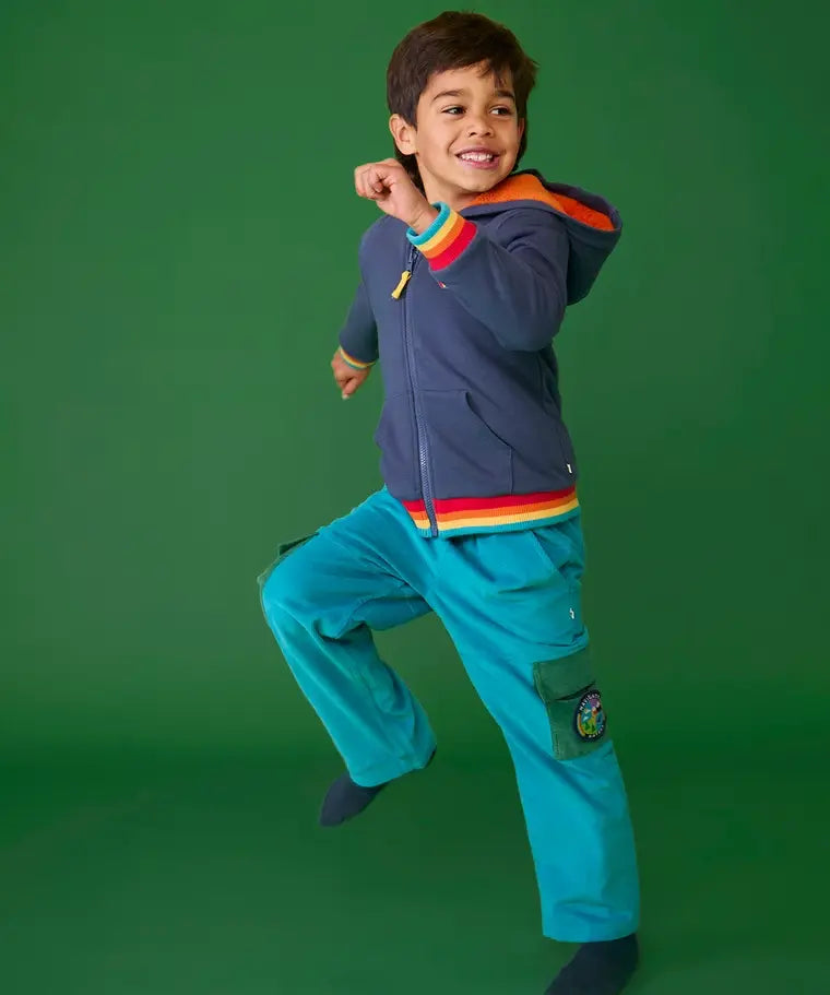 Frugi adventure trousers in boat blue with navy hoodie and rainbow cuffs worn by boy.