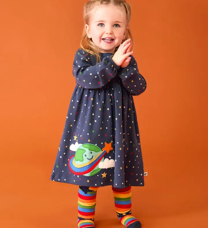 Frugi dolice dress in space and star design worn by little girl with rainbow tights.