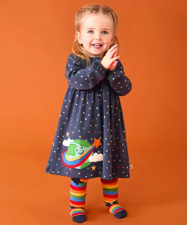 Frugi dolice dress in space and star design worn by little girl with rainbow tights.