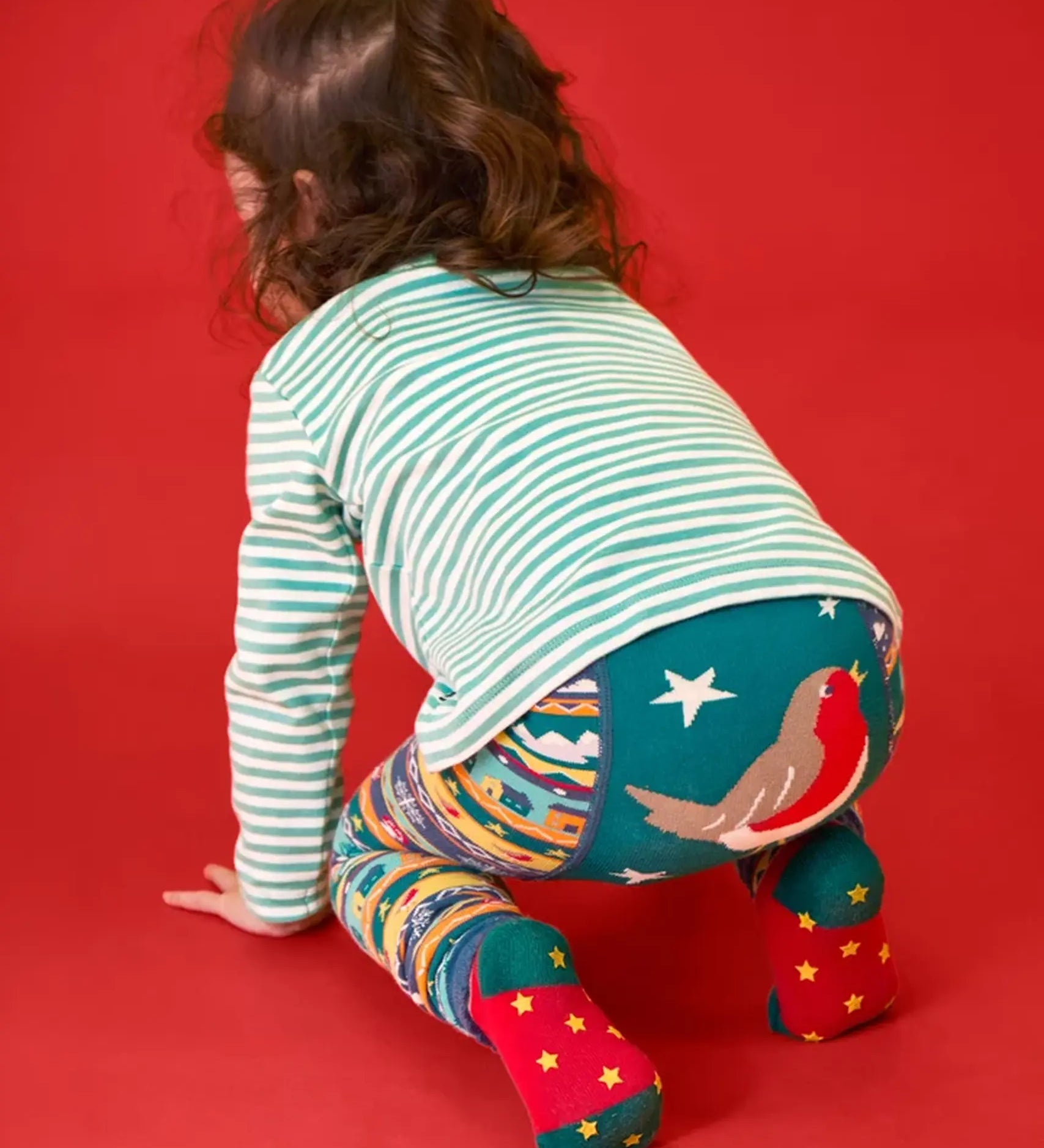 Child crawling away wearing the Frugi GOTS organic knitted footless leggings with a festive fair isle design with large robin on the back.