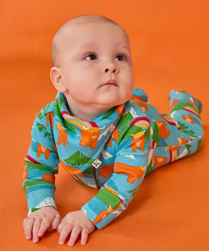 Frugi lovely baby set, a babygrow and matching dribble bib, in blue Highland cow print worn by baby.
