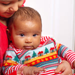 A child looking forwards wearing the Frugi Lumi Knitted Romper - Fairisle Christmas Stripe, sitting with another child