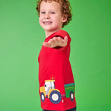 Frugi organic cotton Scout top in red with yellow tractor and green trailer, worn by child with curly hair.