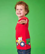 Frugi organic cotton Scout top in red with yellow tractor and green trailer, worn by child with curly hair.