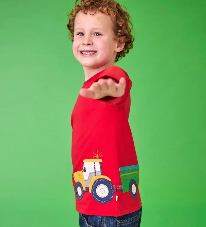 Frugi organic cotton Scout top in red with yellow tractor and green trailer, worn by child with curly hair.