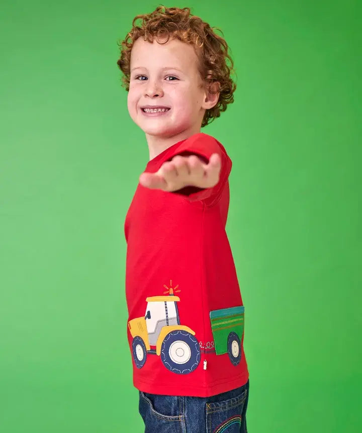Frugi organic cotton Scout top in red with yellow tractor and green trailer, worn by child with curly hair.