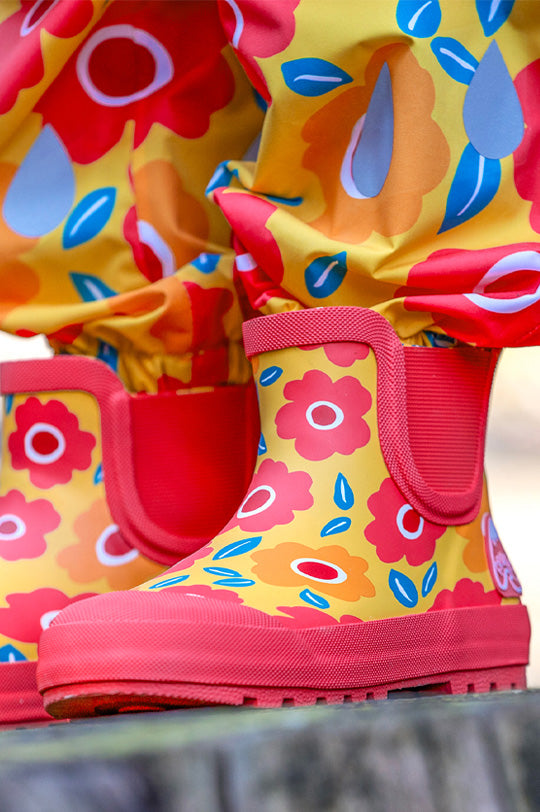 Frugi Rain Or Shine Short waterproof natural rubber Welly Boots in pink and yellow Floral Fields print worn by child to represent Frugi outerwear at Babipur.