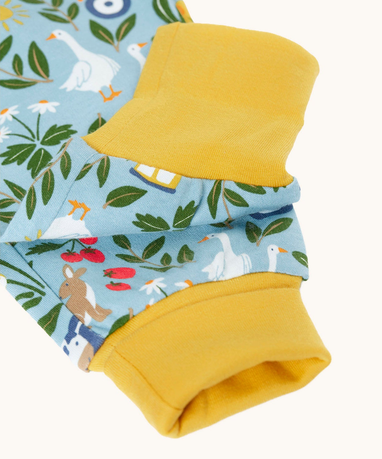 Close up of the light blue Frugi organic cotton dungarees with repeated farm themed print laid flat. Showing the yellow elasticated cuff