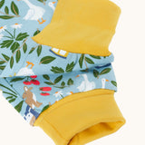 Close up of the light blue Frugi organic cotton dungarees with repeated farm themed print laid flat. Showing the yellow elasticated cuff