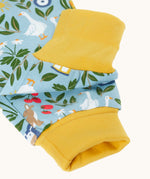 Close up of the light blue Frugi organic cotton dungarees with repeated farm themed print laid flat. Showing the yellow elasticated cuff