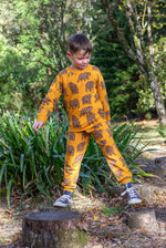 A child playing on tree stumps and wearing the Frugi beary wild parsnip joggers and matching sweater available at Babipur. 