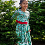 A child standing between two trees and wearing the the Frugi party skater dress in festive forest available at Babipur showing the red tie around the waist
