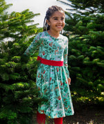 A child standing between two trees and wearing the the Frugi party skater dress in festive forest available at Babipur showing the red tie around the waist