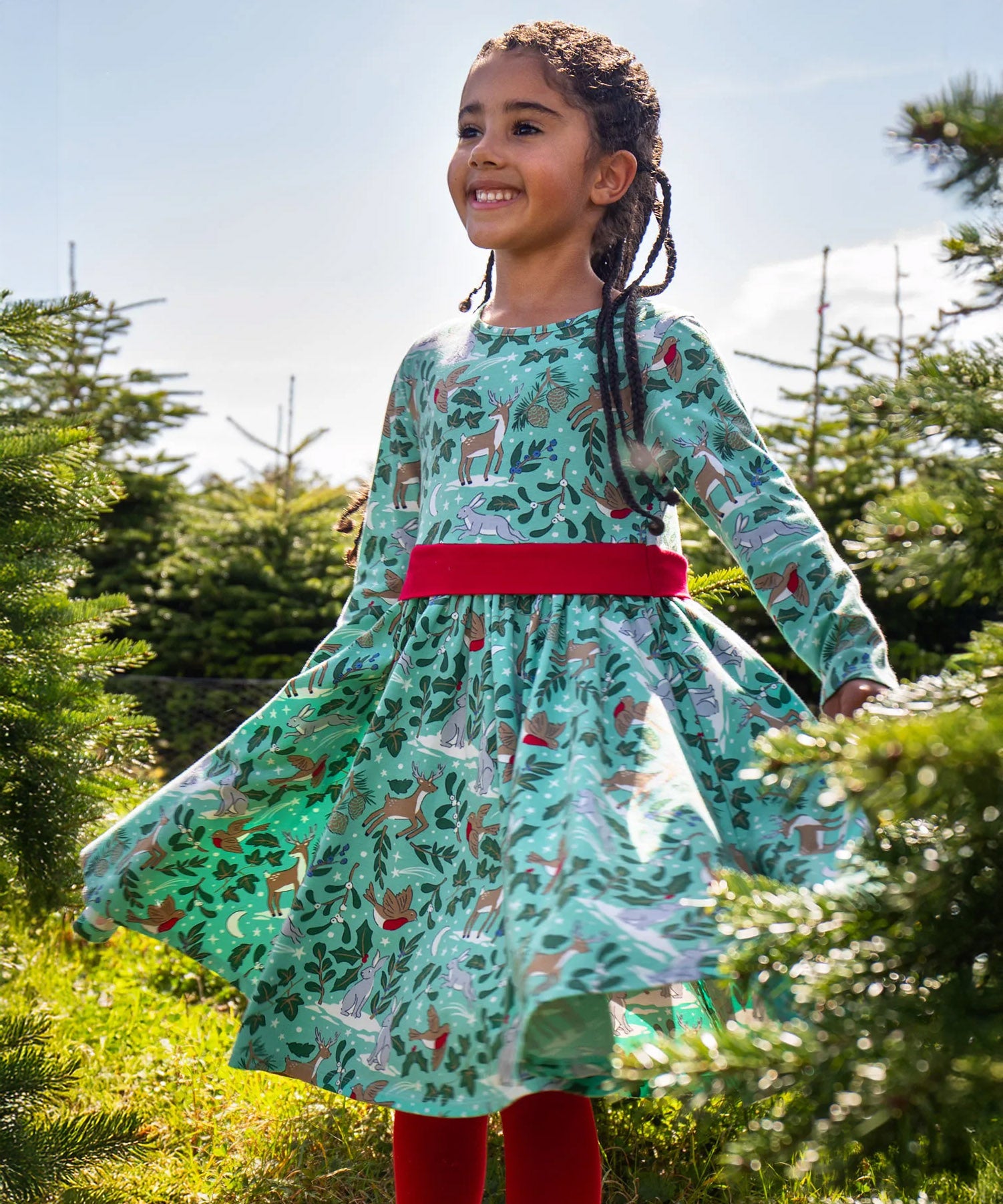 A child standing in the middle of a forest and wearing the the Frugi party skater dress in festive forest available at Babipur showing the gather of the dress