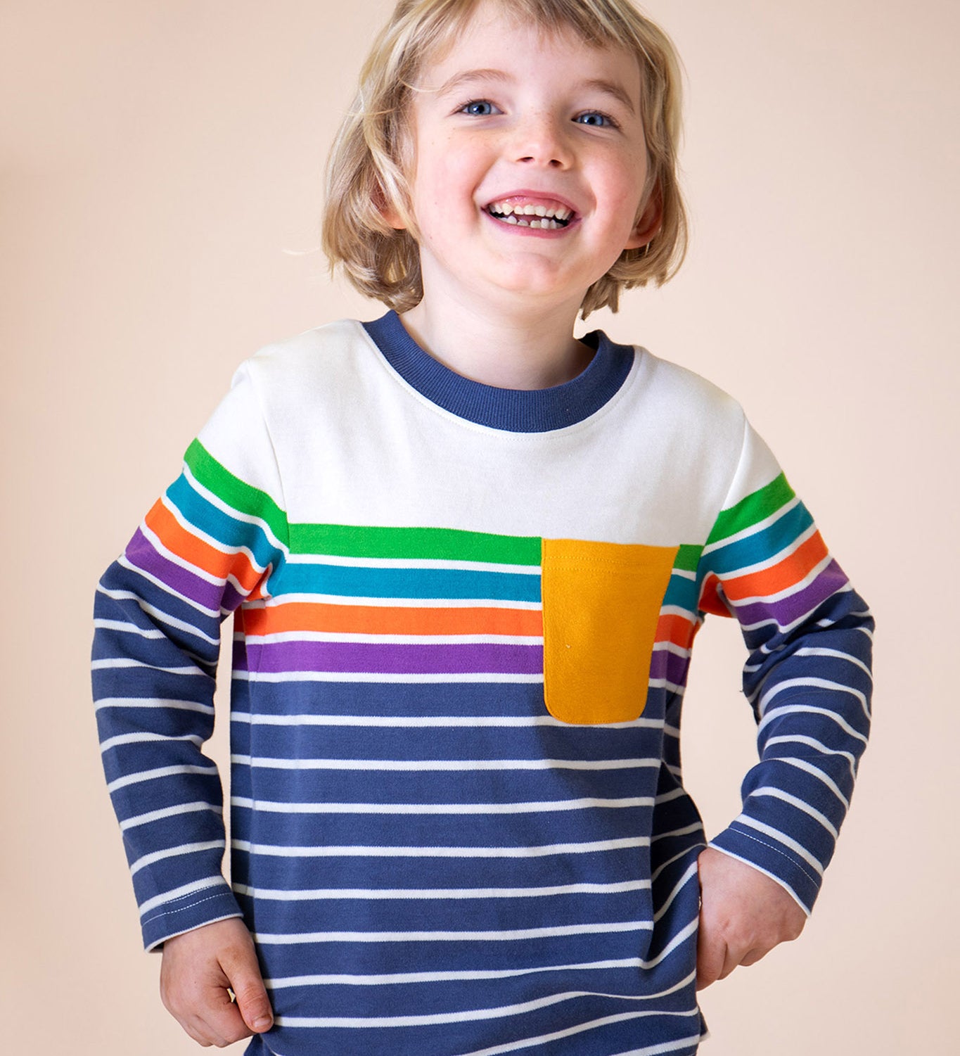 A child wearing the Frugi Piran pocket top in navy stripe available at Babipur. A GOTS organic cotton long sleeved top in a striped design. Features a yellow chest pocket