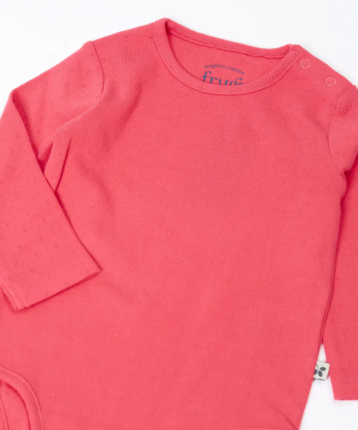 Frugi baby GOTS organic cotton pointelle body laid flat showing the popper fasteners on the shoulder for easy dressing on pink organic cotton fabric 