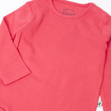 Frugi baby GOTS organic cotton pointelle body laid flat showing the popper fasteners on the shoulder for easy dressing on pink organic cotton fabric 