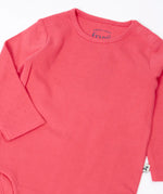 Frugi baby GOTS organic cotton pointelle body laid flat showing the popper fasteners on the shoulder for easy dressing on pink organic cotton fabric 
