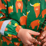 Small child wearing Frugi's waterproof puddle buster coat in highland grazing showing close up of the repeating Highland cow design 